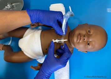 Both hands holding the new tracheostomy tube with one thumb over the obturator as it is being inserted