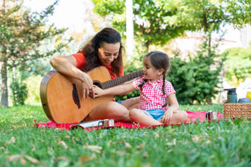 Child and adult playing guitar at a picnic