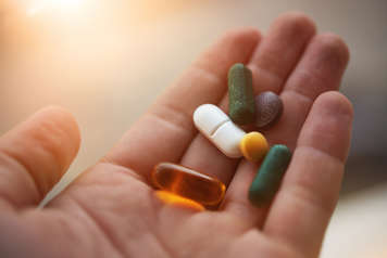Hand holding of various vitamin tablets and pills