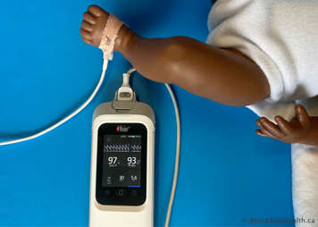 Baby with oximeter probe wrapped around their foot and readings showing a baseline