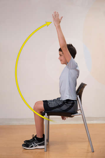 side view of boy sitting in chair with arm raised above him