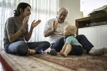 Mother and grandfather clapping and playing with baby on the floor