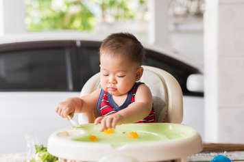 baby sitting in high chair playing with food