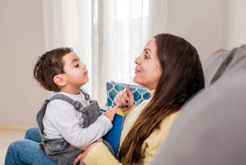Toddler sitting on woman's lap on a couch. They are facing each other and have their chins tilted up slightly